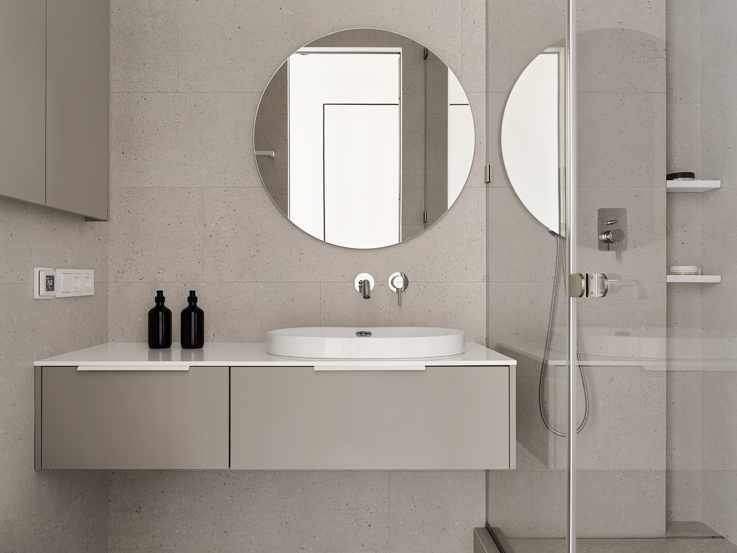 Guest bathroom with round mirror, wall-mounted vanity, and travertine-look tiles